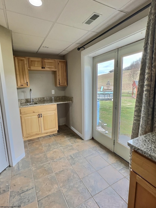 kitchen featuring light stone counters, a drop ceiling, and sink