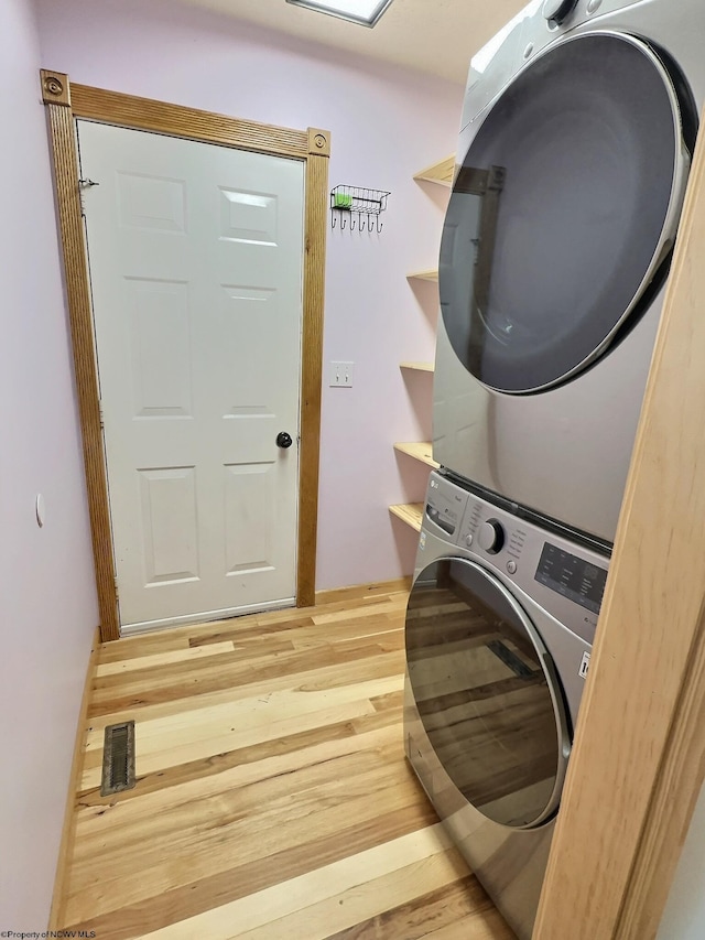 clothes washing area with hardwood / wood-style flooring and stacked washing maching and dryer