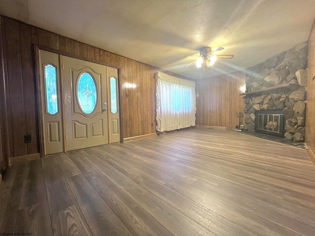 foyer entrance with ceiling fan, wood walls, wood-type flooring, a textured ceiling, and a fireplace