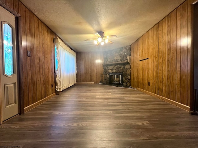 unfurnished living room featuring a wealth of natural light, dark wood-type flooring, a stone fireplace, and a textured ceiling