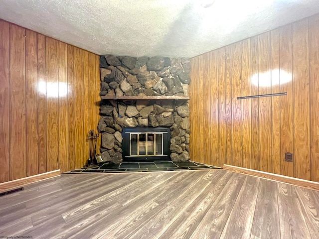 unfurnished living room featuring hardwood / wood-style flooring, a fireplace, wooden walls, and a textured ceiling