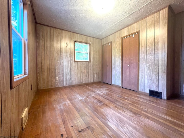 unfurnished bedroom with wood walls, light hardwood / wood-style floors, a textured ceiling, and two closets