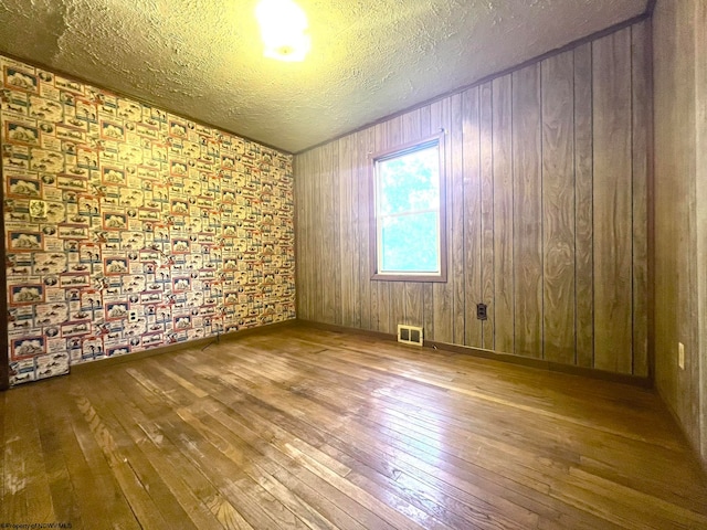 empty room with hardwood / wood-style floors, wooden walls, and a textured ceiling