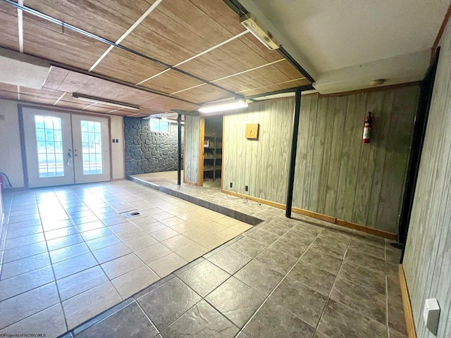 basement featuring french doors, wooden ceiling, tile patterned floors, and wooden walls