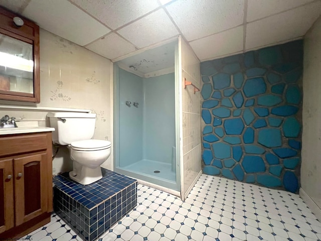 bathroom with a paneled ceiling, walk in shower, vanity, and toilet