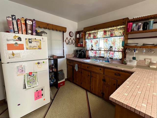 kitchen with dark brown cabinets, sink, white refrigerator, and tile counters