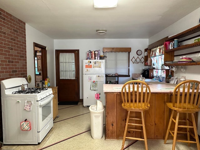 kitchen featuring white appliances, brick wall, a breakfast bar area, and kitchen peninsula