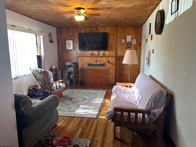 living room with ceiling fan, wood-type flooring, and wood walls