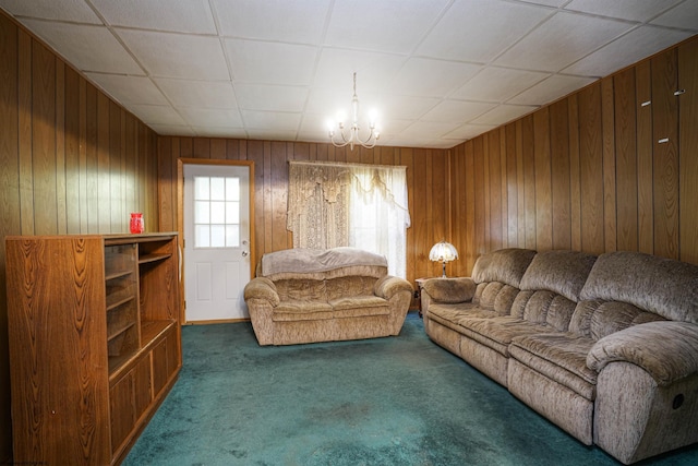 carpeted living room featuring a chandelier, wooden walls, and a drop ceiling