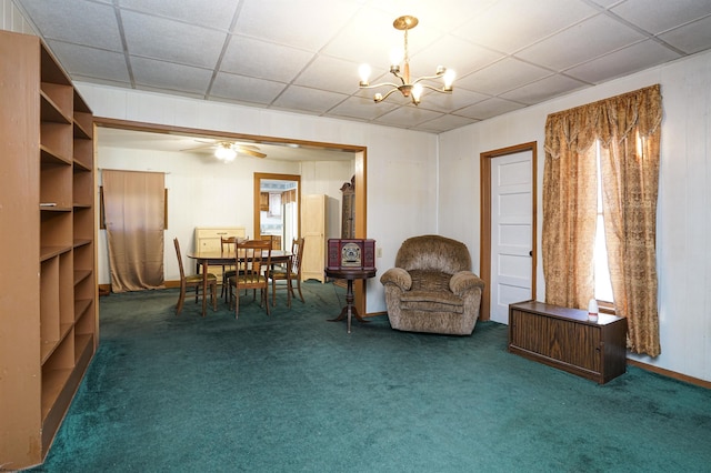 living area with a paneled ceiling, dark carpet, and ceiling fan with notable chandelier