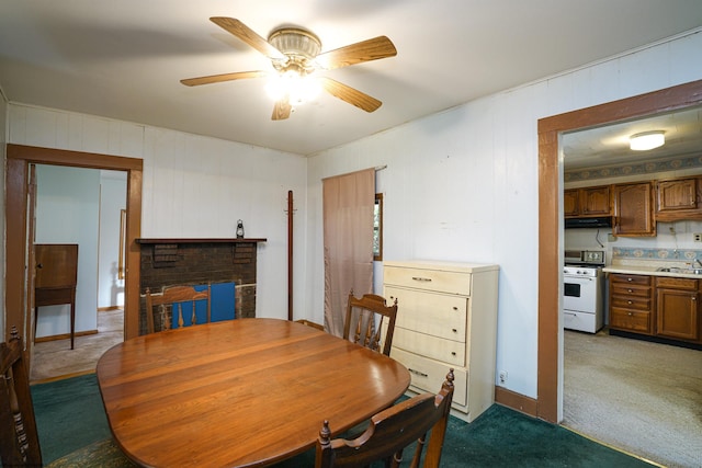 dining area with ceiling fan, a fireplace, sink, and dark carpet