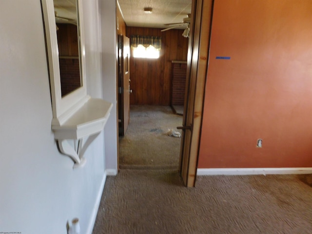 hallway featuring wood walls, a textured ceiling, and dark carpet