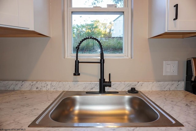 interior details with light stone countertops, sink, and white cabinets