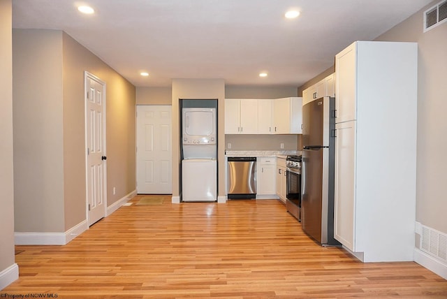 kitchen featuring light hardwood / wood-style flooring, white cabinets, stainless steel appliances, and stacked washer / dryer