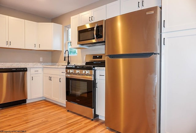 kitchen with light stone countertops, appliances with stainless steel finishes, white cabinetry, and light wood-type flooring