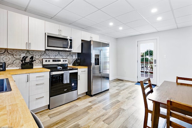 kitchen featuring appliances with stainless steel finishes, a drop ceiling, light wood-type flooring, and backsplash