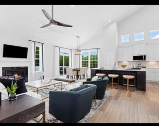 living room with a wealth of natural light, ceiling fan with notable chandelier, light hardwood / wood-style flooring, and high vaulted ceiling