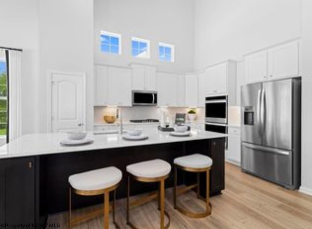 kitchen with a kitchen bar, a towering ceiling, appliances with stainless steel finishes, an island with sink, and white cabinets