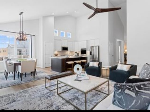 living room with high vaulted ceiling, ceiling fan with notable chandelier, and light hardwood / wood-style flooring