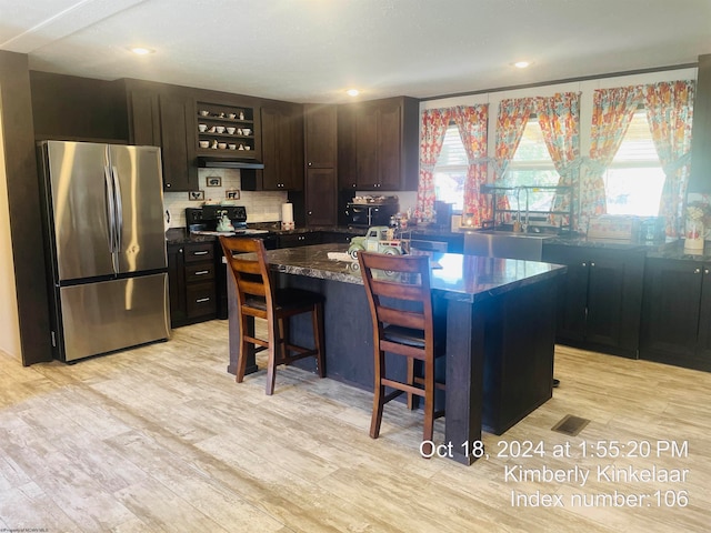 kitchen featuring a breakfast bar, dark brown cabinets, a kitchen island, light hardwood / wood-style flooring, and stainless steel refrigerator