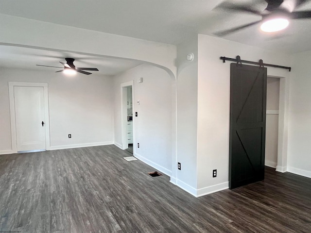 unfurnished room with ceiling fan, a barn door, and dark wood-type flooring