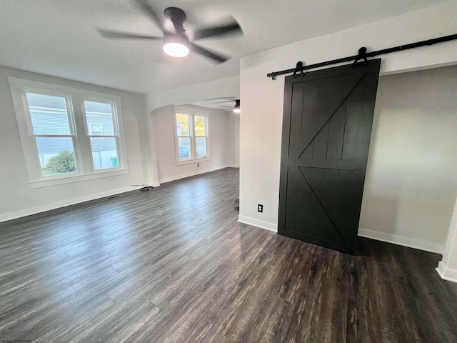 empty room with a barn door, ceiling fan, and dark hardwood / wood-style flooring