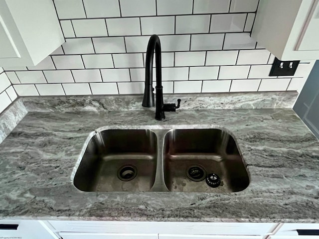 interior details featuring tasteful backsplash, sink, white cabinets, and stone countertops