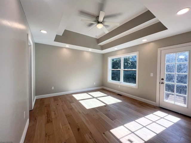 unfurnished room featuring light hardwood / wood-style flooring, a tray ceiling, and ceiling fan