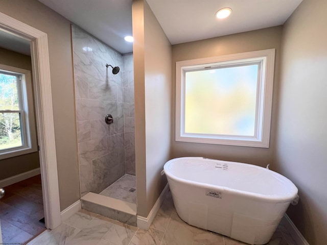 bathroom featuring marble finish floor, tiled shower, a freestanding bath, and baseboards