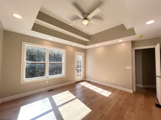 unfurnished room with a raised ceiling, light wood-style flooring, and baseboards