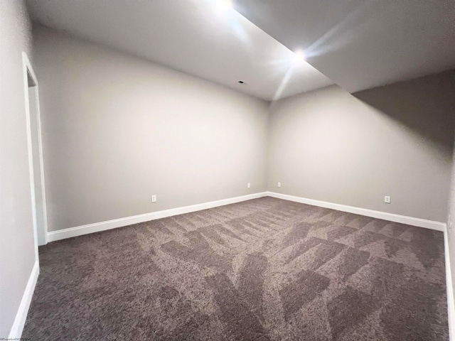 spare room featuring dark carpet and baseboards