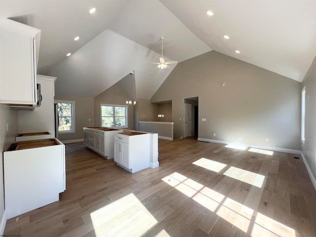 kitchen featuring high vaulted ceiling, light wood-style flooring, ceiling fan with notable chandelier, white cabinets, and open floor plan