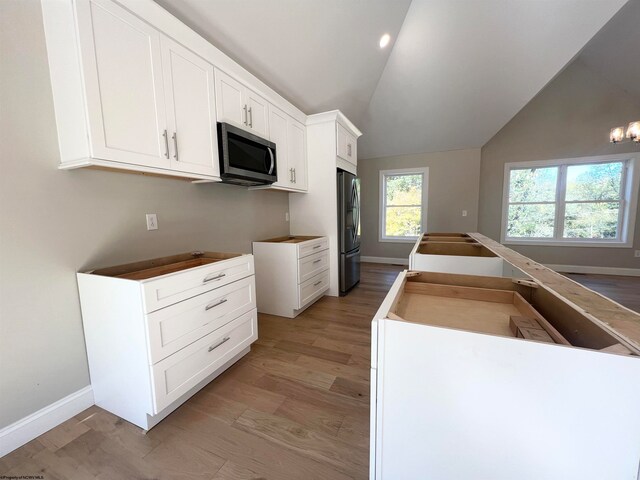 kitchen featuring lofted ceiling, baseboards, white cabinets, light wood-style floors, and appliances with stainless steel finishes