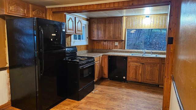 kitchen featuring ornamental molding, sink, black appliances, light wood-type flooring, and wood walls