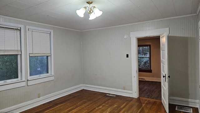 empty room featuring a notable chandelier, ornamental molding, and dark hardwood / wood-style flooring