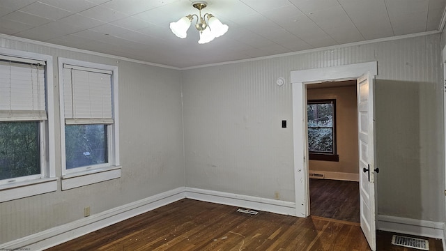 unfurnished room with wood-type flooring, a notable chandelier, ornamental molding, and visible vents