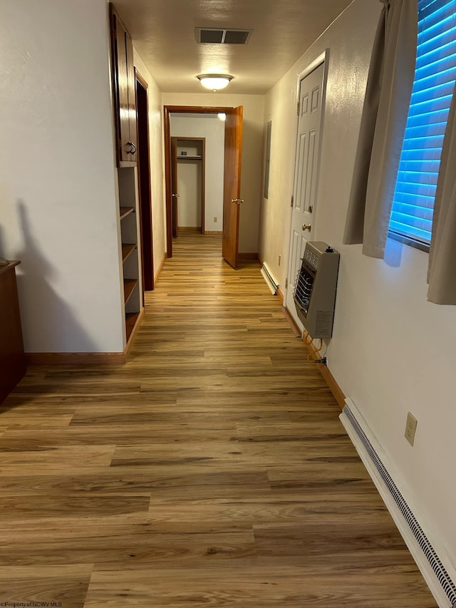 corridor featuring baseboard heating, heating unit, and hardwood / wood-style flooring