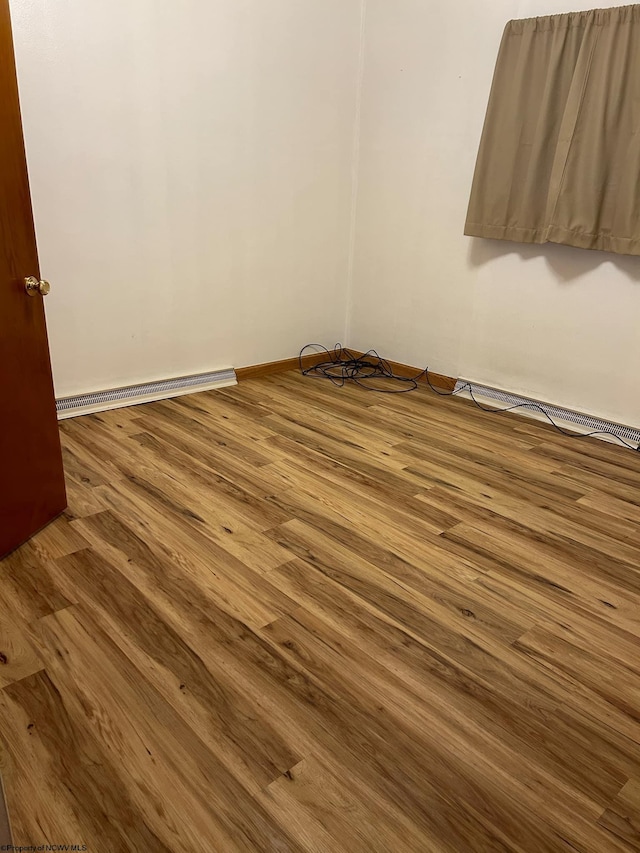 empty room featuring wood-type flooring and a baseboard radiator