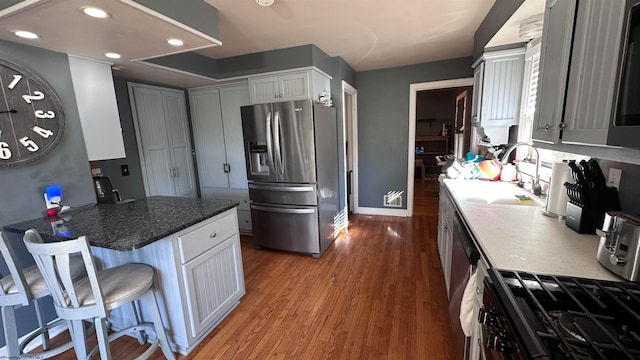 kitchen featuring wood-type flooring, sink, a breakfast bar, white cabinetry, and appliances with stainless steel finishes