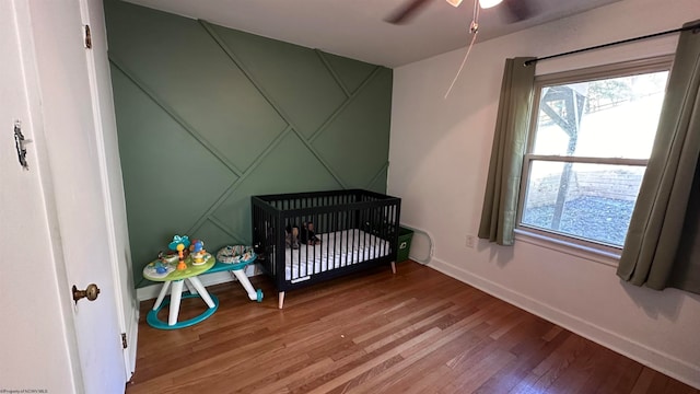 bedroom featuring ceiling fan, wood-type flooring, and a crib