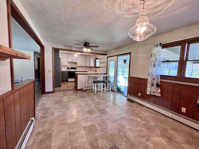 kitchen with electric range oven, hanging light fixtures, baseboard heating, white cabinets, and a breakfast bar area