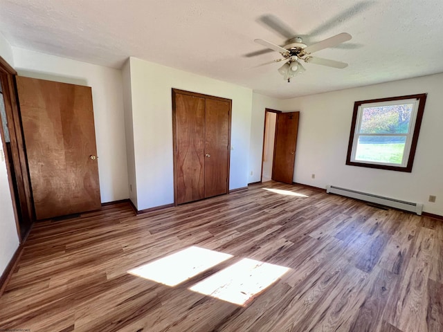 unfurnished bedroom featuring baseboard heating, a textured ceiling, light wood-type flooring, and ceiling fan