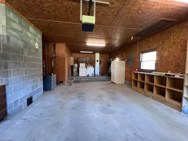 garage with water heater, electric panel, washing machine and dryer, and white refrigerator