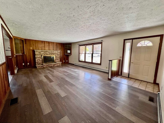 unfurnished living room featuring wood walls, a baseboard heating unit, a textured ceiling, and hardwood / wood-style floors