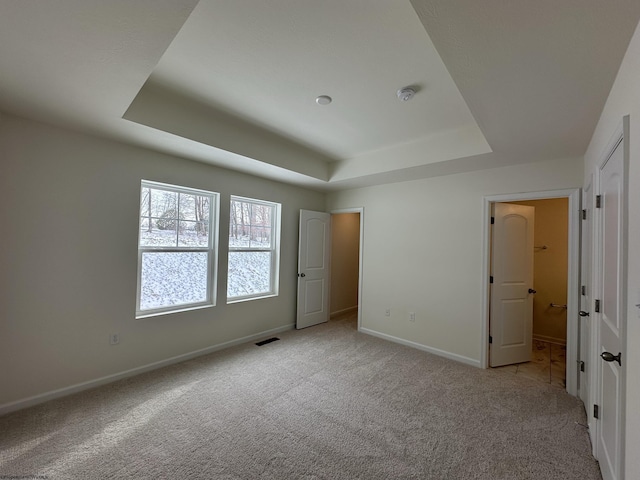 unfurnished bedroom featuring a raised ceiling and light carpet