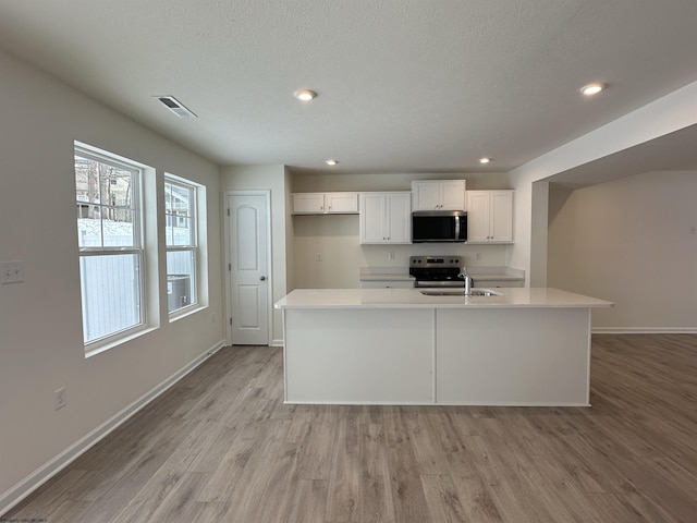 kitchen with sink, stainless steel appliances, a center island with sink, white cabinets, and light wood-type flooring