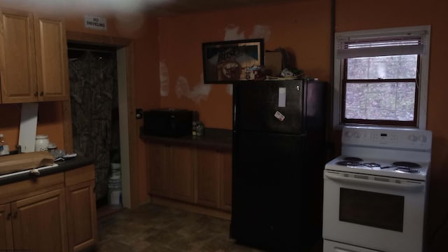 kitchen with dark countertops, white electric stove, light brown cabinetry, and freestanding refrigerator