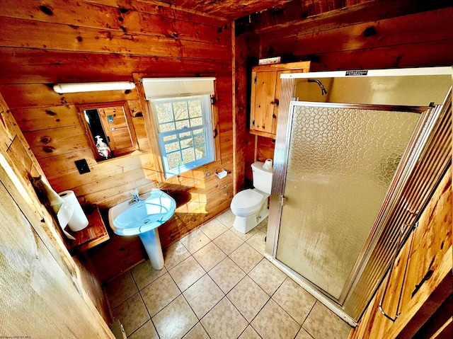 bathroom featuring a shower with door, wooden walls, toilet, and tile patterned flooring