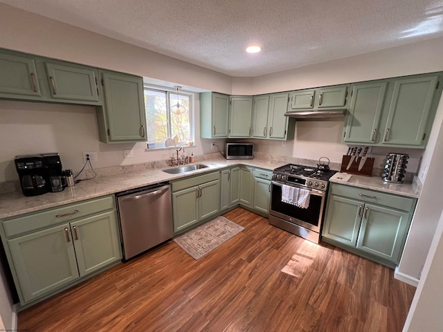 kitchen with dark wood-type flooring, stainless steel appliances, sink, green cabinetry, and a textured ceiling