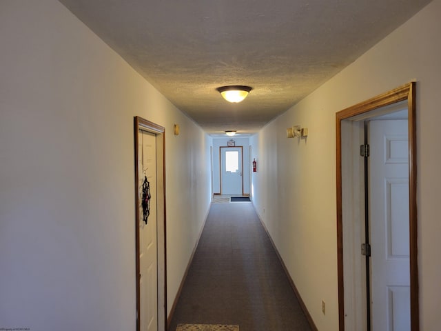 hall with dark carpet and a textured ceiling